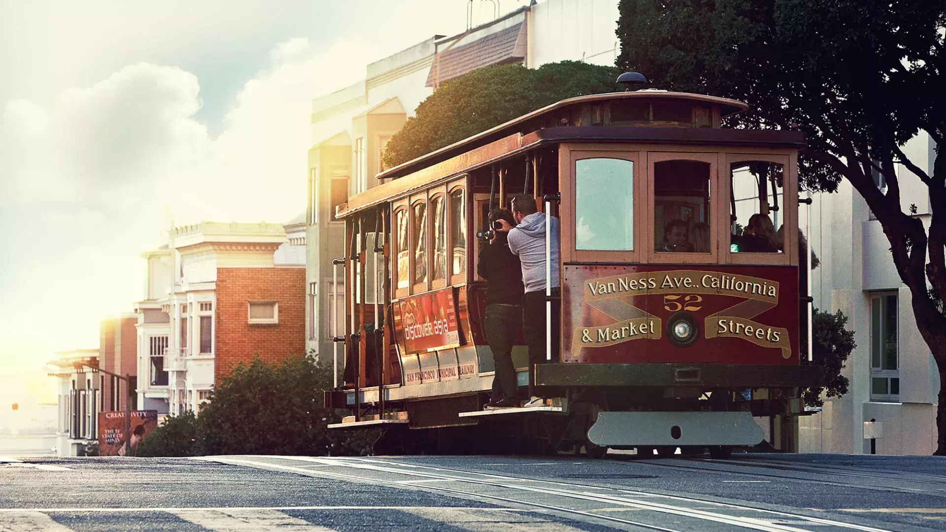 A cable car rounds a hill in San Francisco with passengers looking out the window.