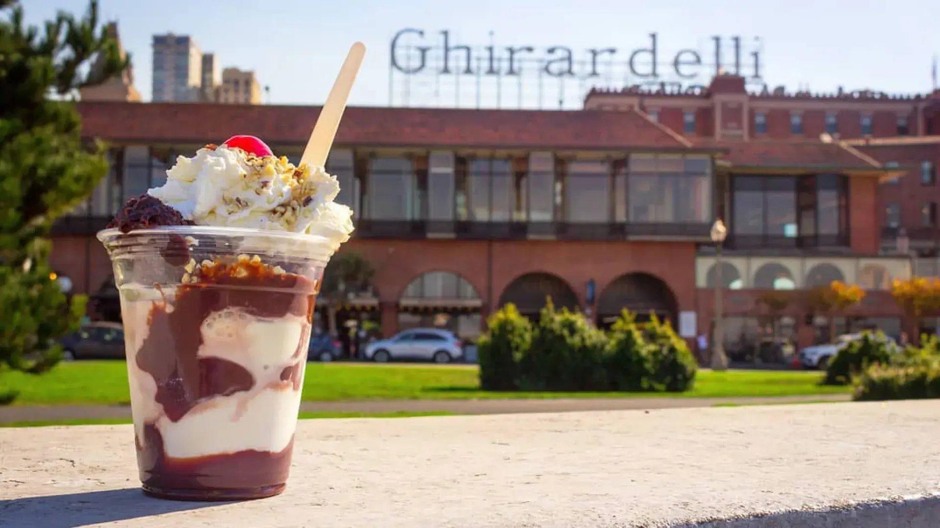 A chocolate sundae sits in the foreground with Ghirardelli Square in the background.