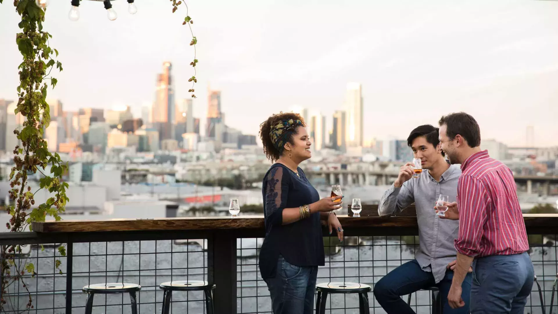 Three people gather around an outdoor table on the roof deck of Anchor Distilling in San Francisco, California.