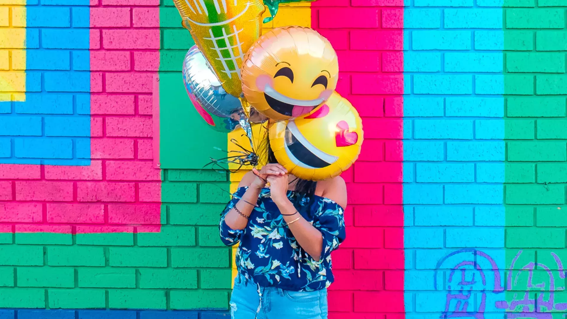 Uma menina comemora seu aniversário com balões em frente a um mural colorido.