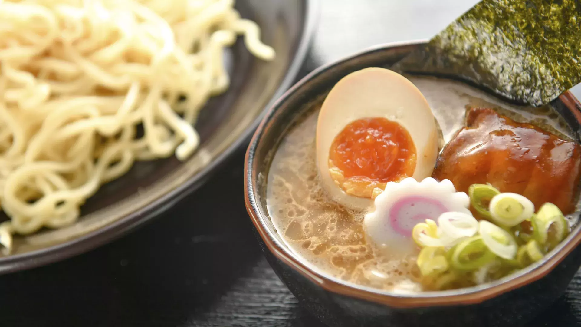 Close-up de uma tigela de macarrão e uma tigela de sopa de ramen com um ovo escalfado, cortado ao meio.