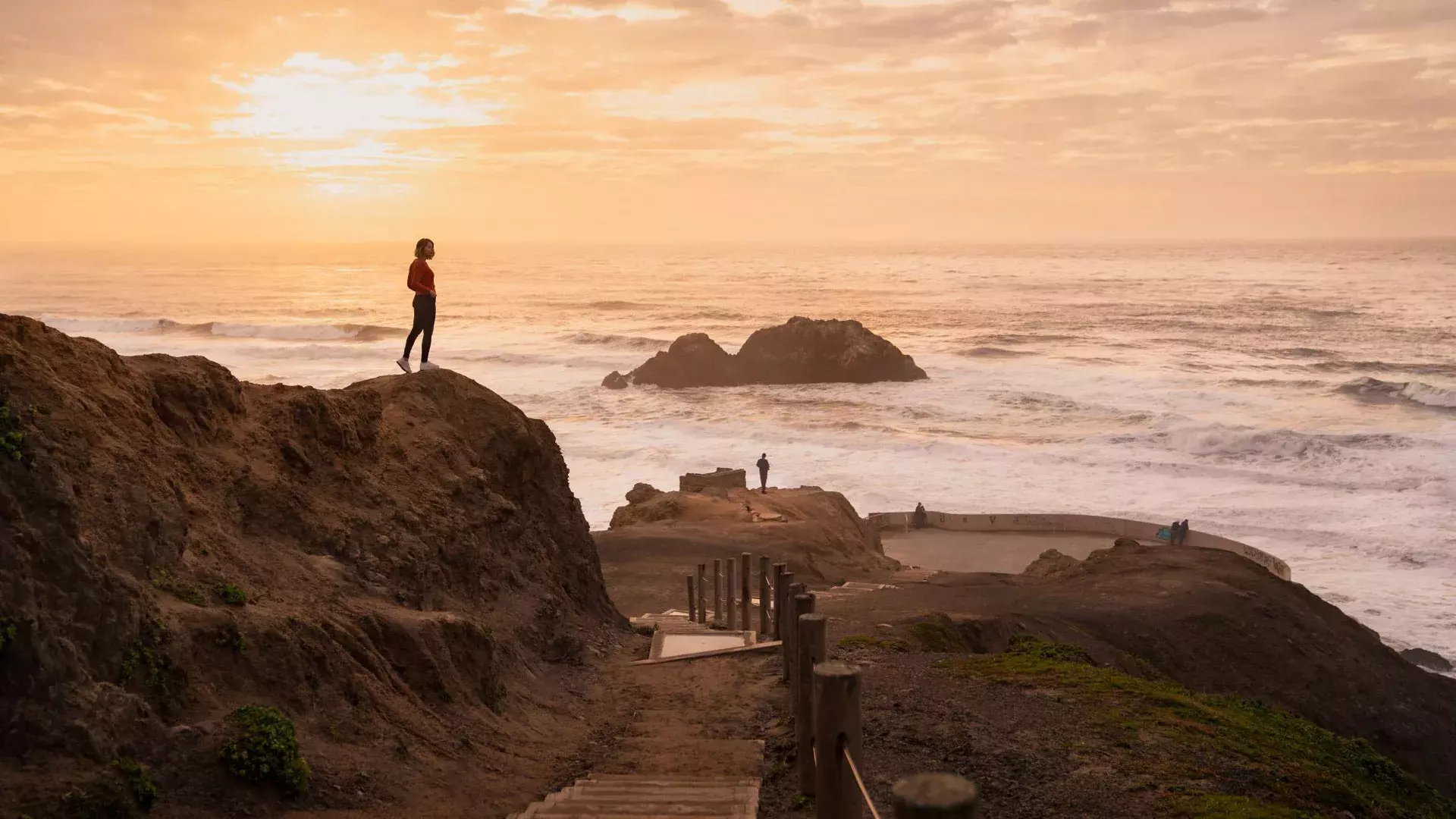 Two people stand on rocks overlooking the ocean at Sutro Baths in San Francisco.