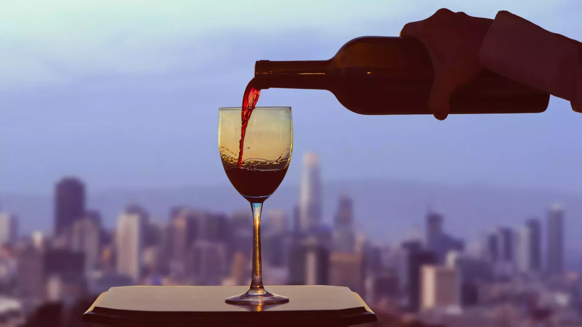 A glass of red wine being poured, with the San Francisco skyline visible out the window.