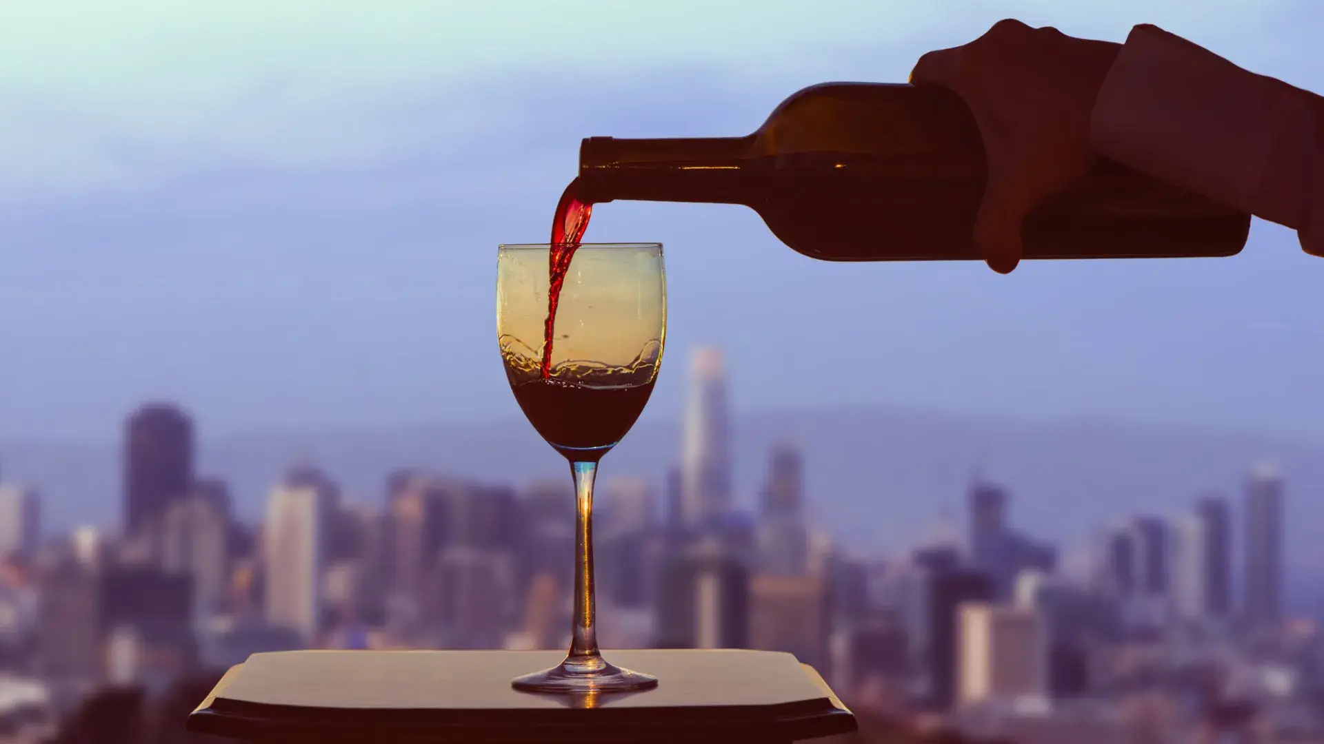 A glass of red wine being poured, with the San Francisco skyline visible out the window.