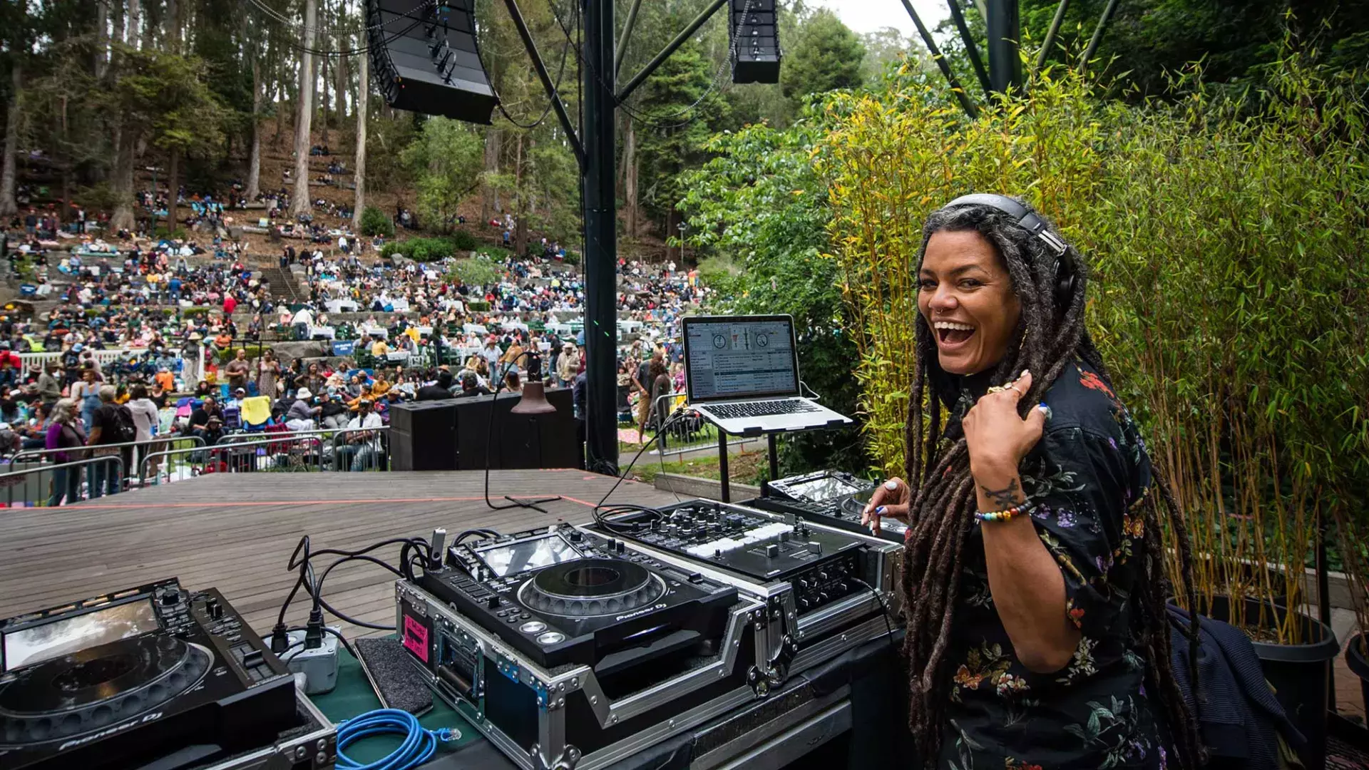 스턴 그로브 페스티벌(Stern Grove Festival)에서 DJ를 하고 있는 한 여성이 어깨 너머로 카메라를 바라보며 미소를 짓고 있습니다.