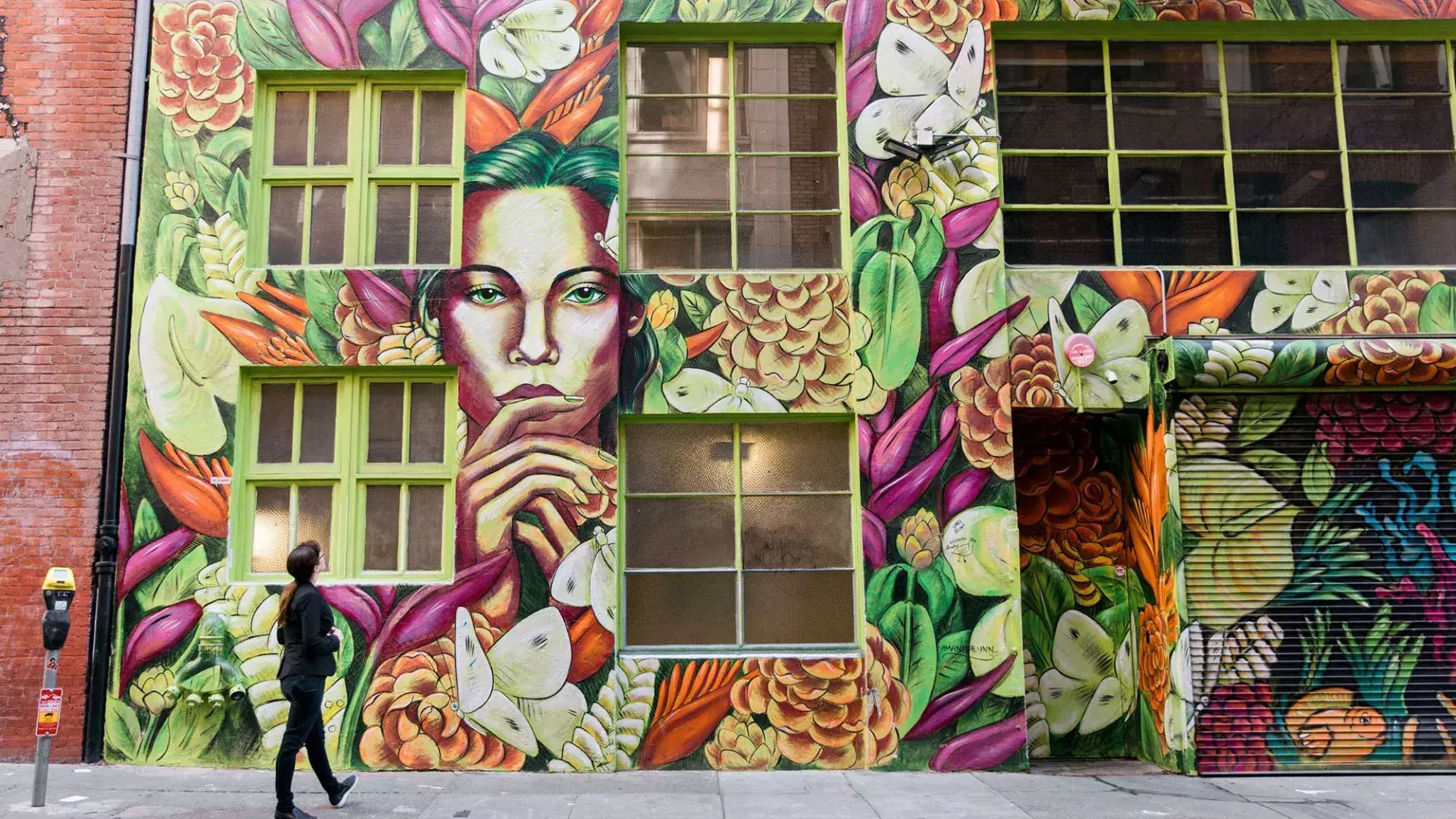 A woman looks up at a brightly colored mural on the side of a brick building in San Francisco.