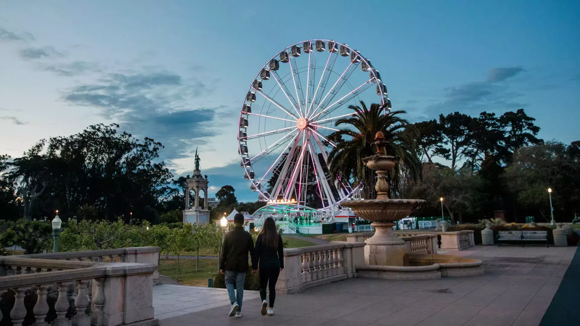 A couple walks toward the SkyStar Ferris Wheel at dusk.