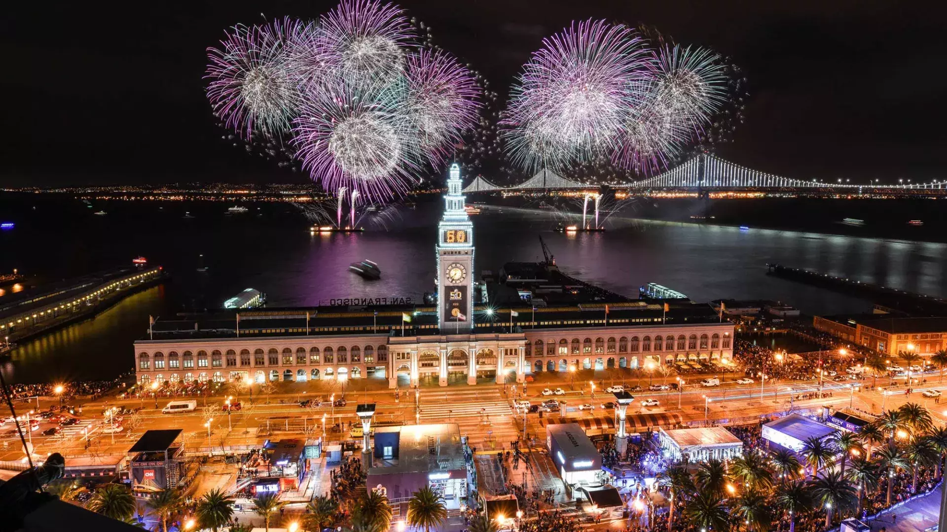 Fireworks explode over top of the Ferry Building, with the Bay Bridge in the background. San Francisco, California.