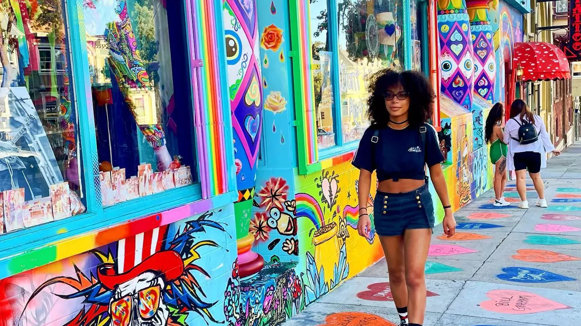 Woman walking down Haight Street with a colorful mural in the background.