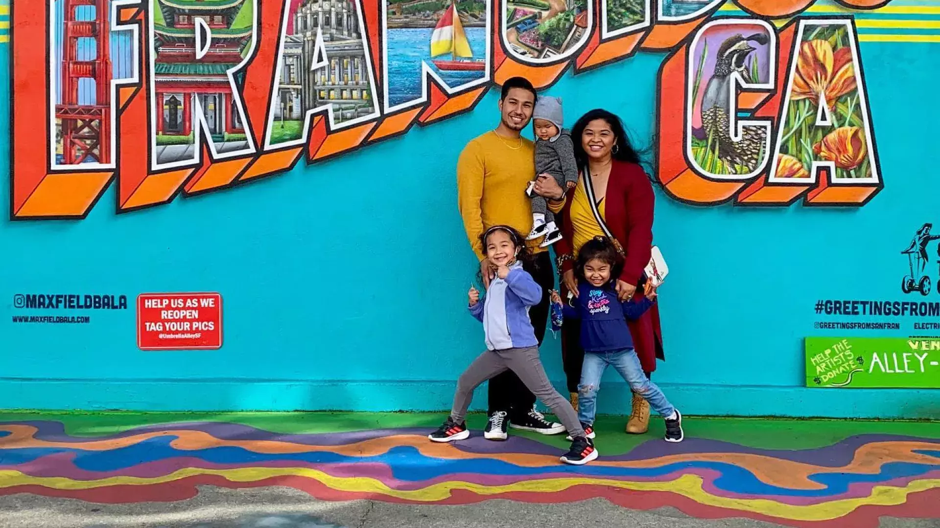 Uma família posando para uma foto em frente a um mural de São Francisco