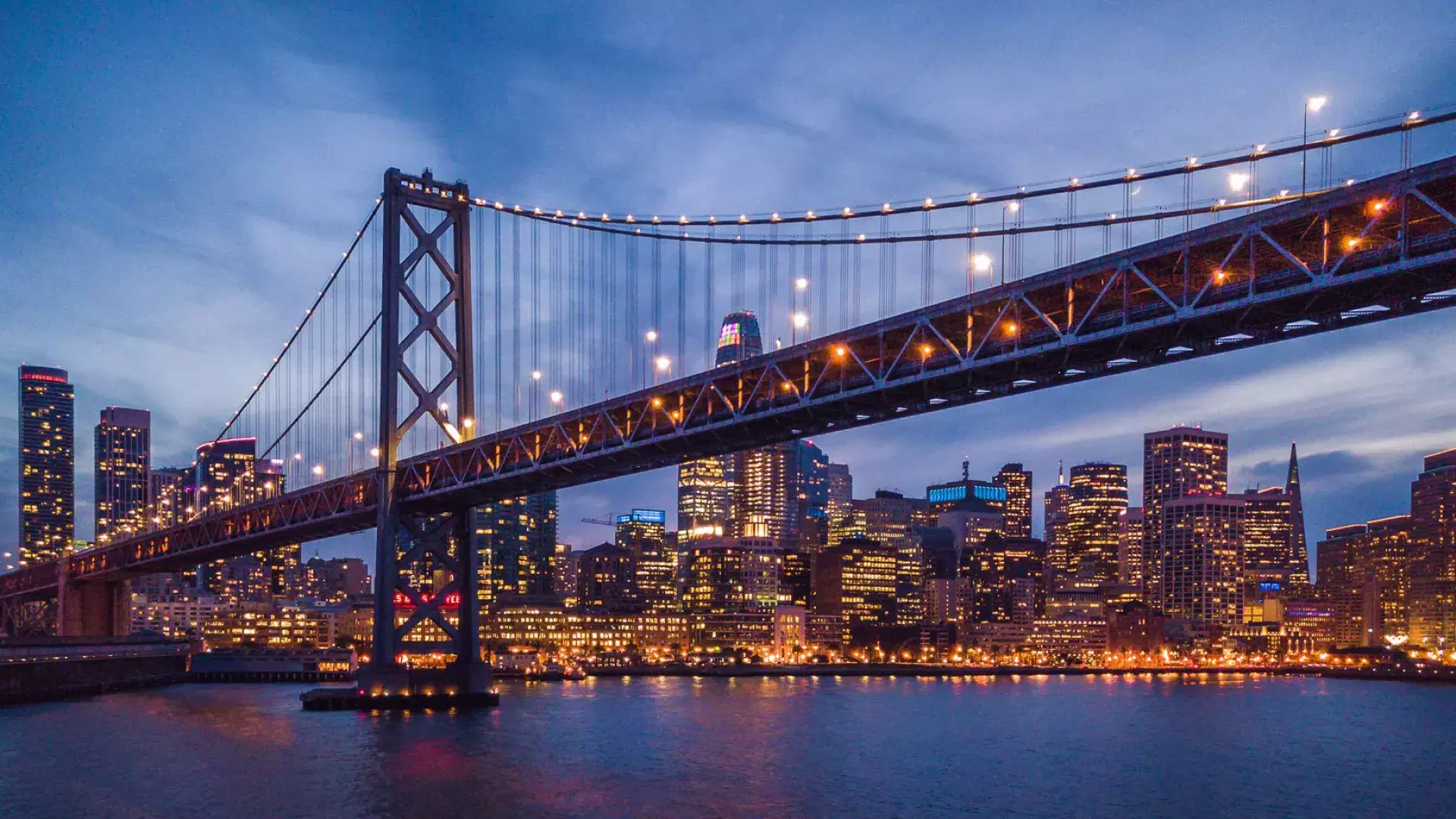 The Bay Bridge and Embarcardero waterfront lit up at night.