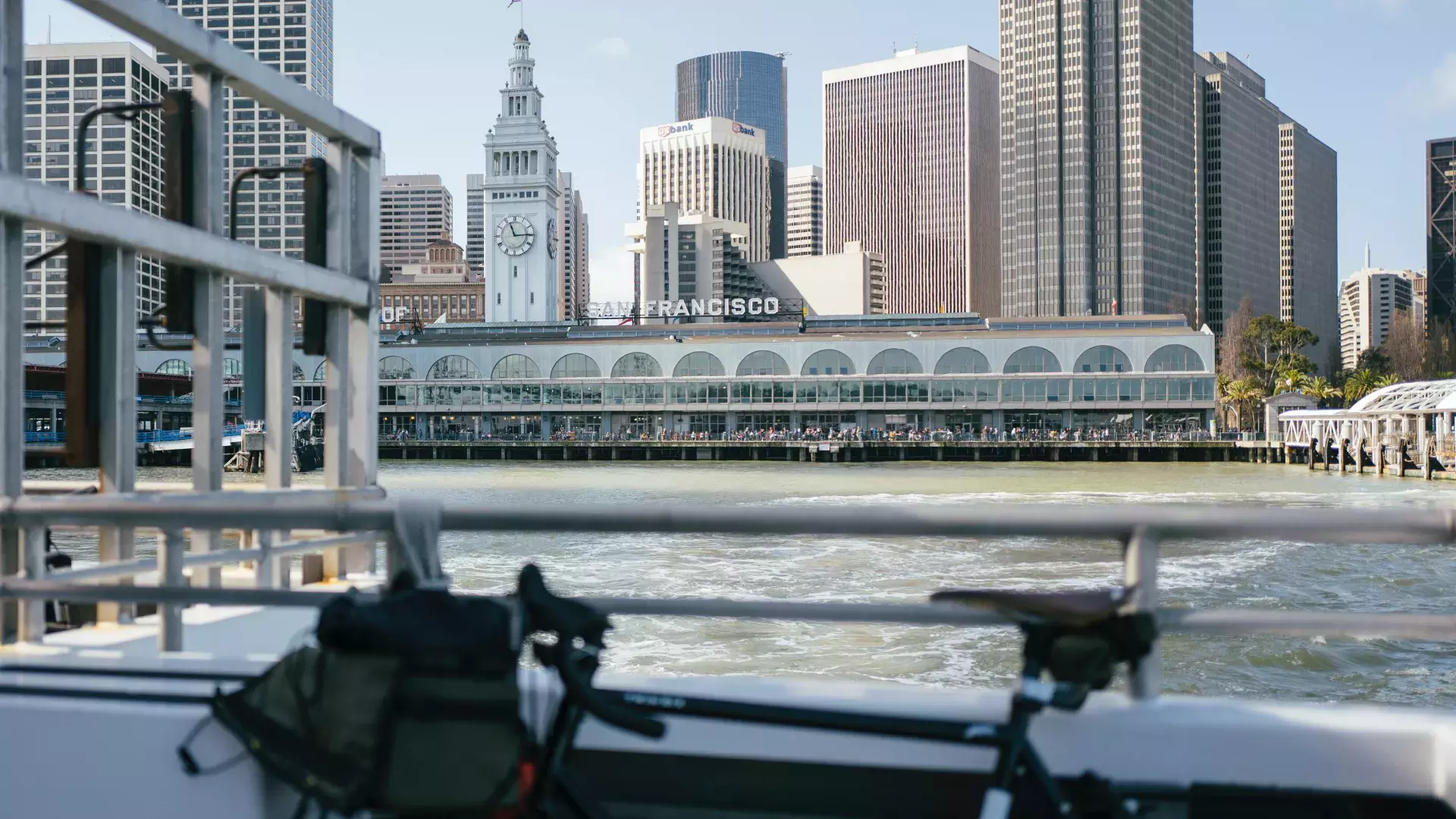 Bicicleta encostada em um trilho com o Ferry Building ao fundo.