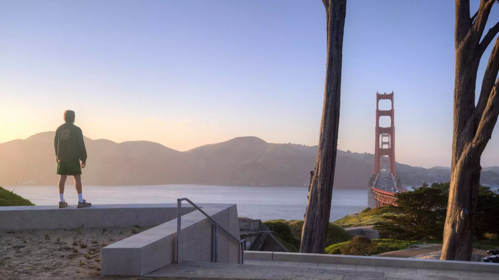 Um homem observa a ponte Golden Gate com montanhas ao fundo.