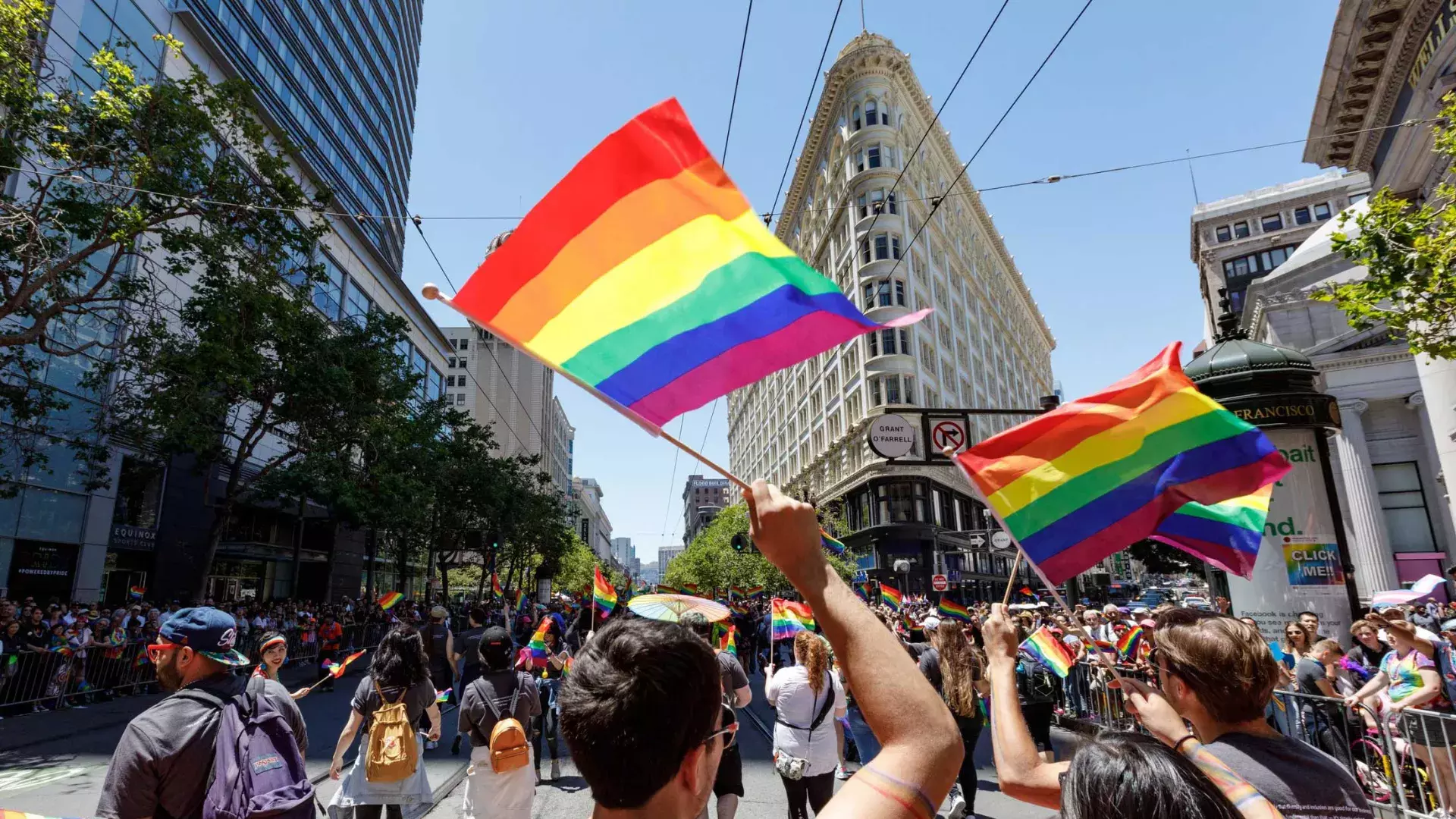 People walking in the San Francisco Pride parade wave rainbow flags.