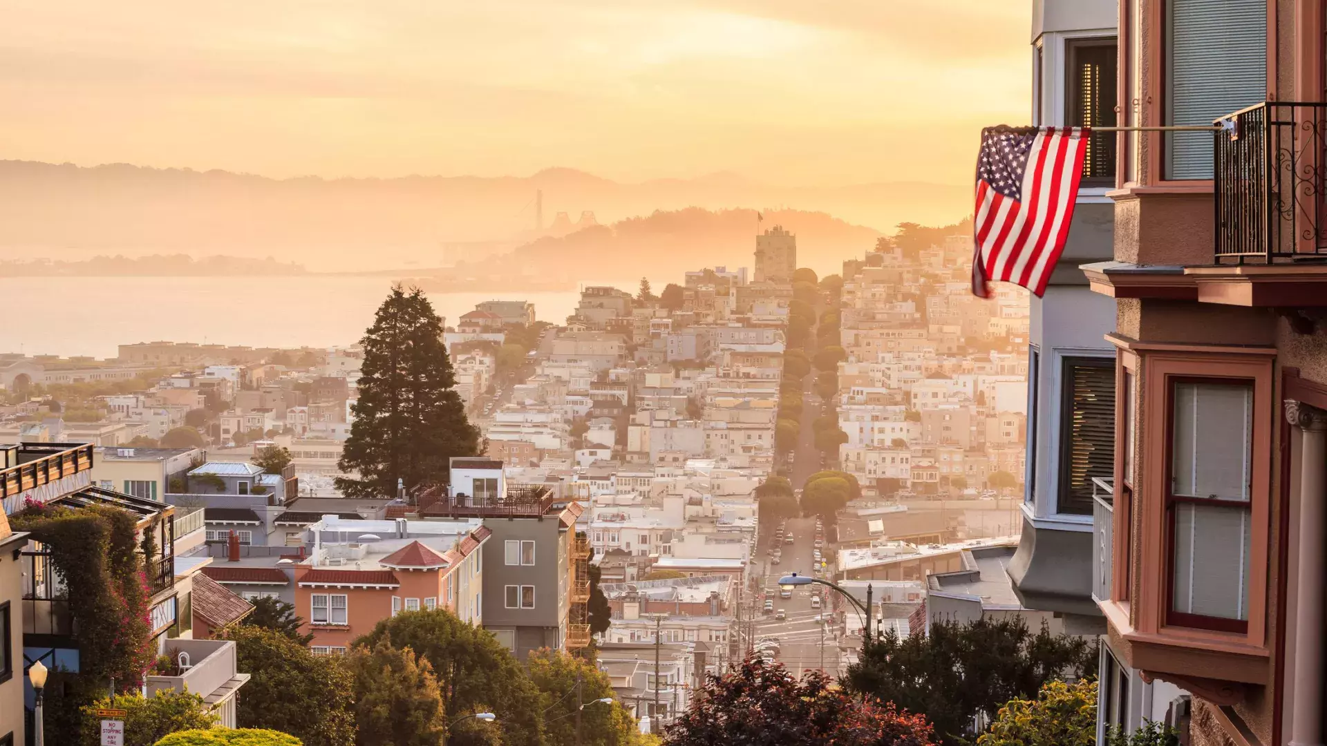 Uma vista de São Francisco do topo de uma colina, com uma bandeira americana tremulando em primeiro plano.