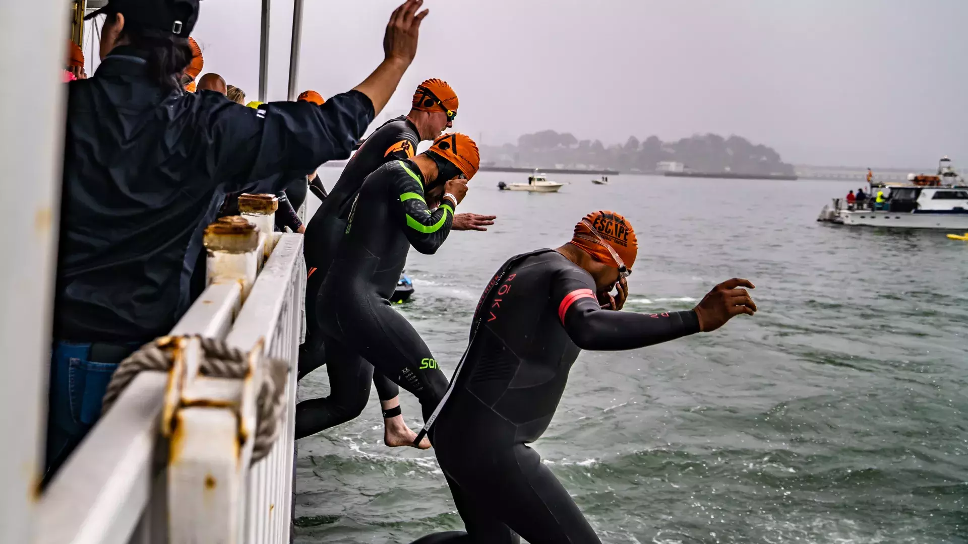 Triathlon participants jumping from a boat into the San Francisco Bay on a Foggy Morning.