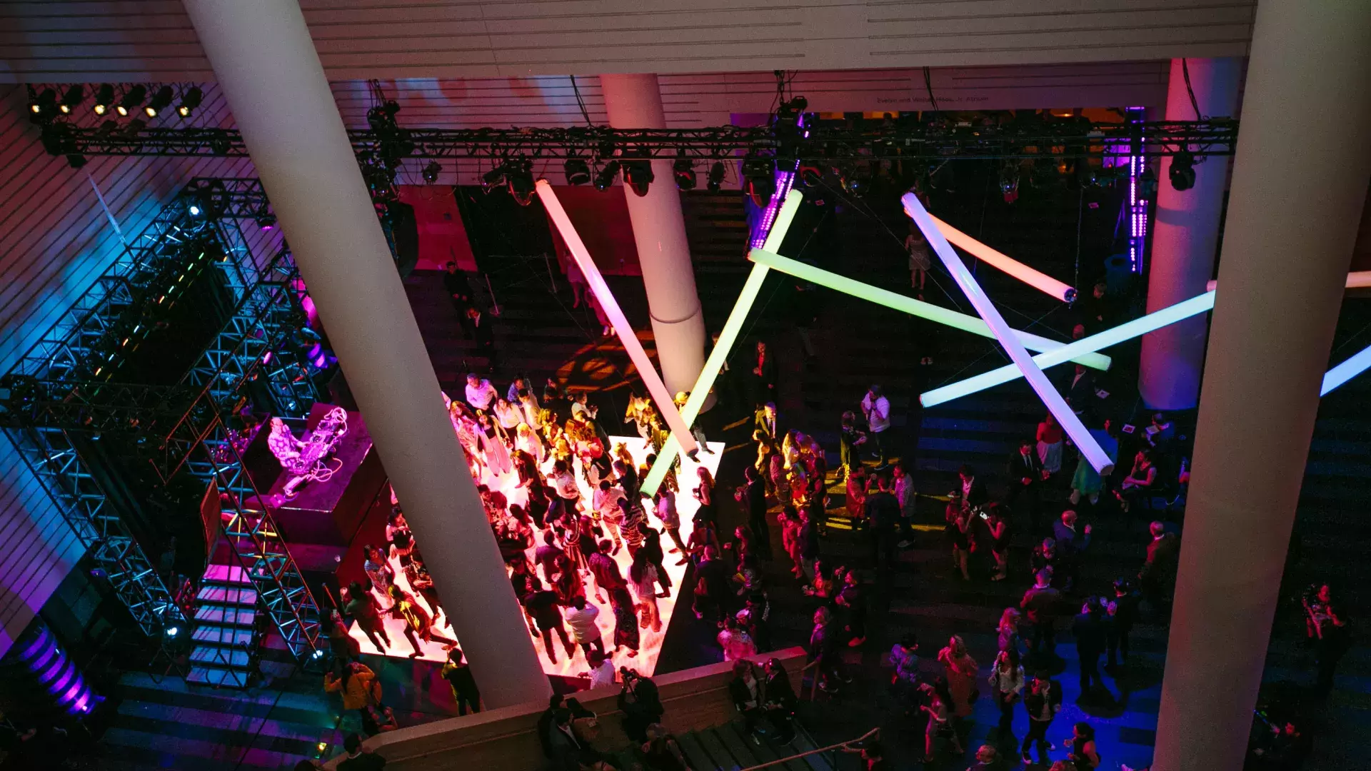 Image of people on a dance floor lit by rainbow neon lights hanging from ceiling