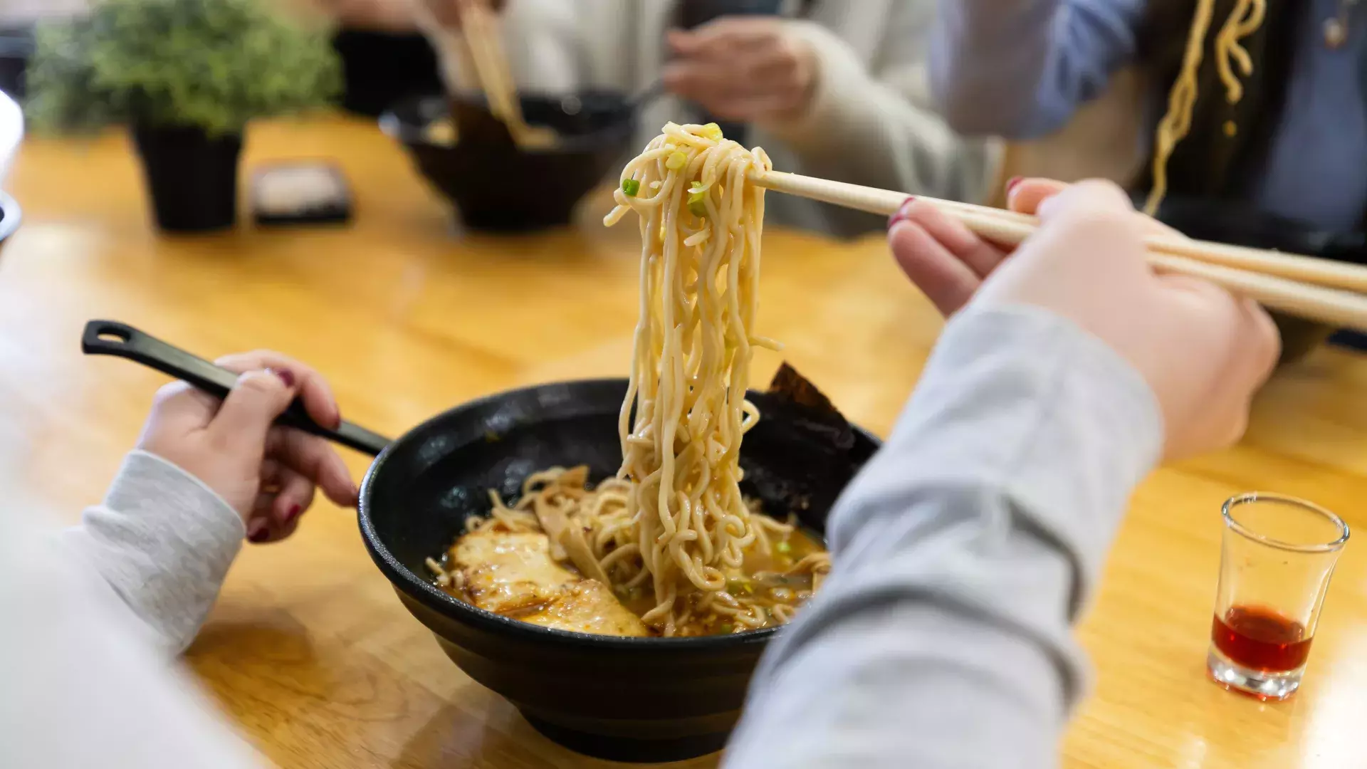 Person lifting ramen noodles out of a bowl with chopsticks
