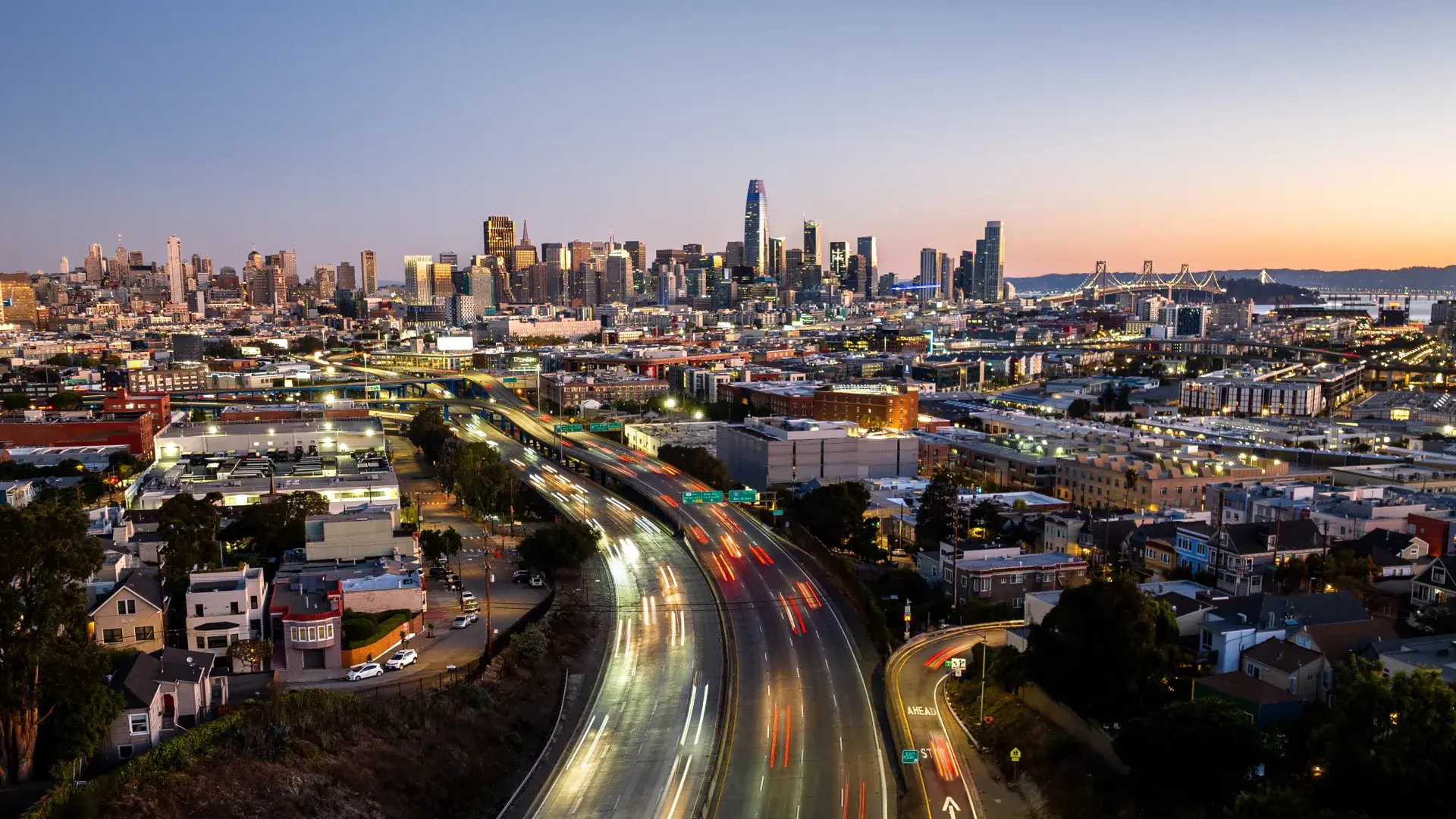 Downtown San Francisco skyline at dusk, with cars rushing on freeway heading in and out of the city.