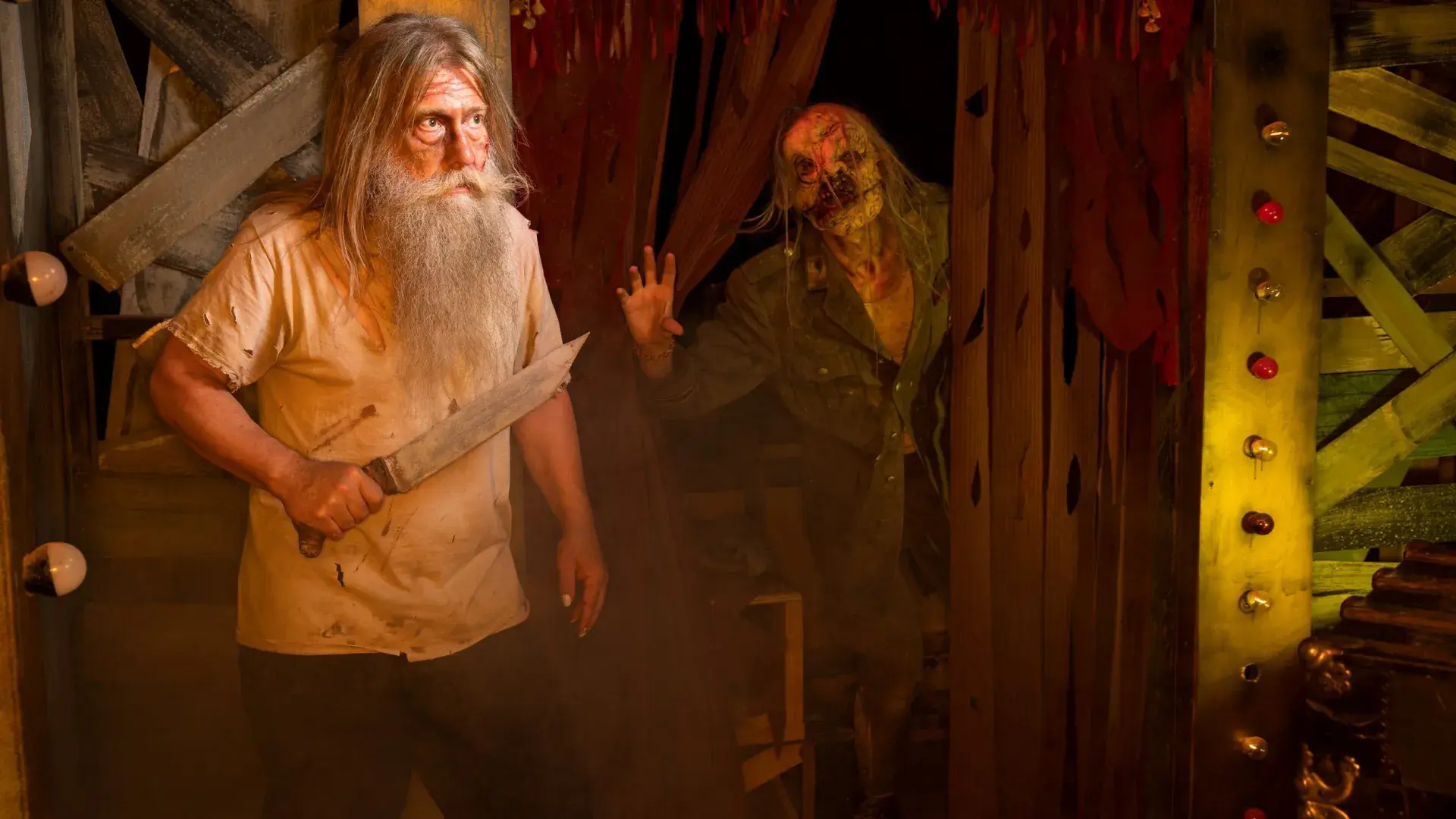Man with long gray beard holding knife with a ghoulish monster behind him 
