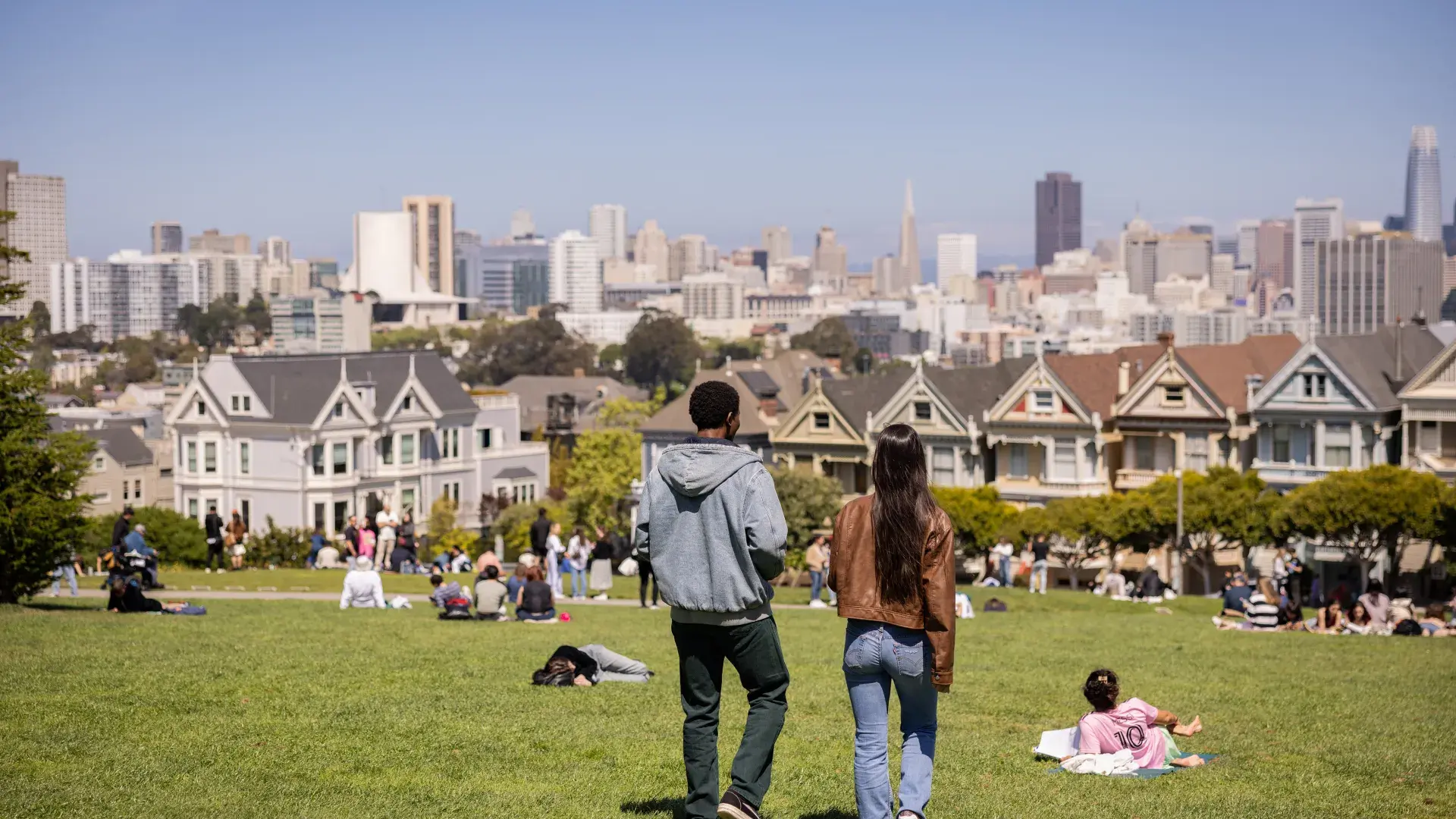 Duas pessoas caminhando em frente às painted ladies no Alamo Square Park