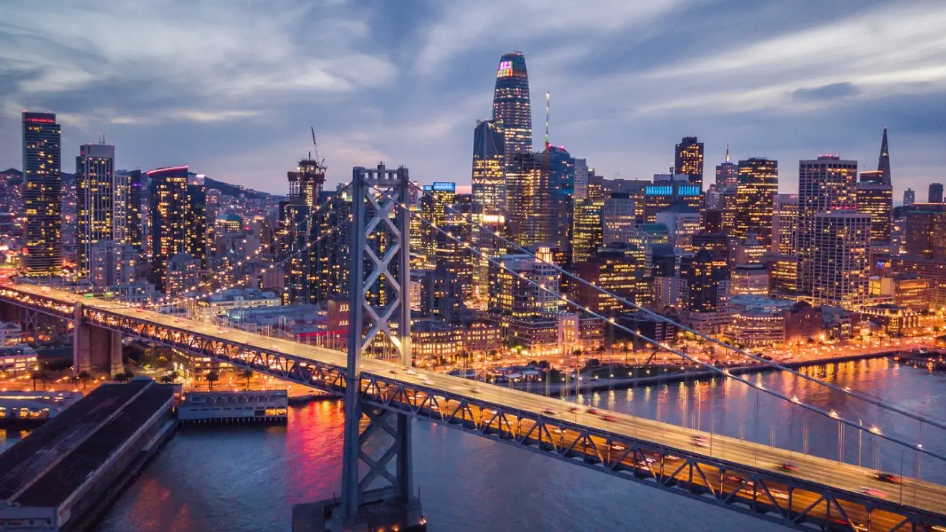 The San Francisco Bay Bridge and city skyline lit up at night.
