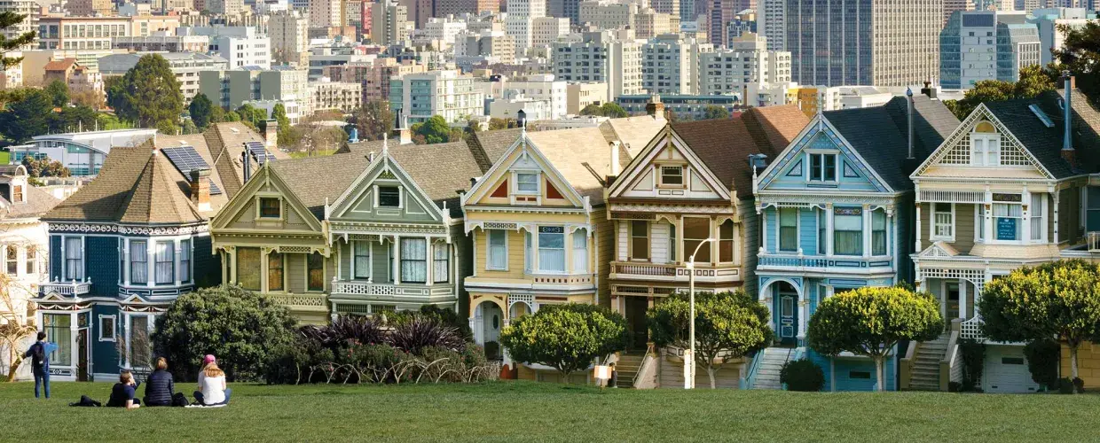 Picnickers sit on the grass at Alamo Square Park with the Painted Ladies and San Francisco skyline in the background.