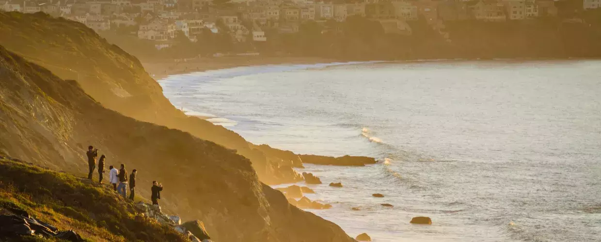A group of people stand on an oceanfront cliffside watching the sunset in San Francisco's Presidio.