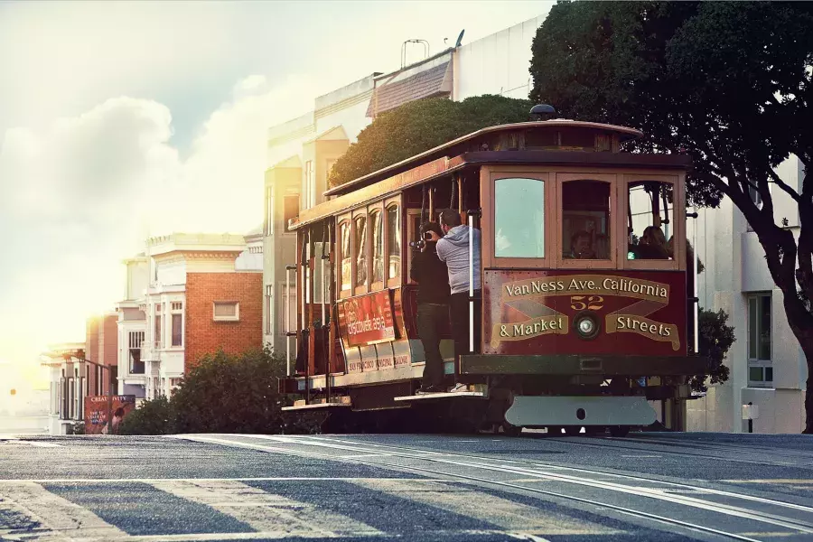 Un téléphérique contourne une colline à San Francisco avec des passagers regardant par la fenêtre.