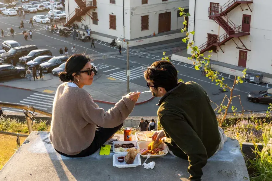 A couple dines al fresco at Fort Mason Center in San Francisco. The woman feeds her companion a taste of food.