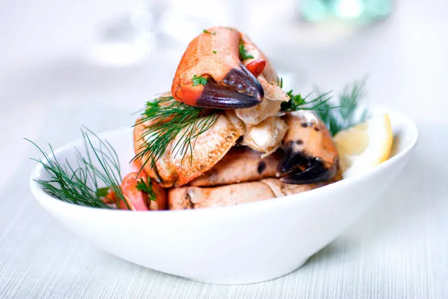 Crab legs are stacked in a white bowl and sprinkled with fresh dill.