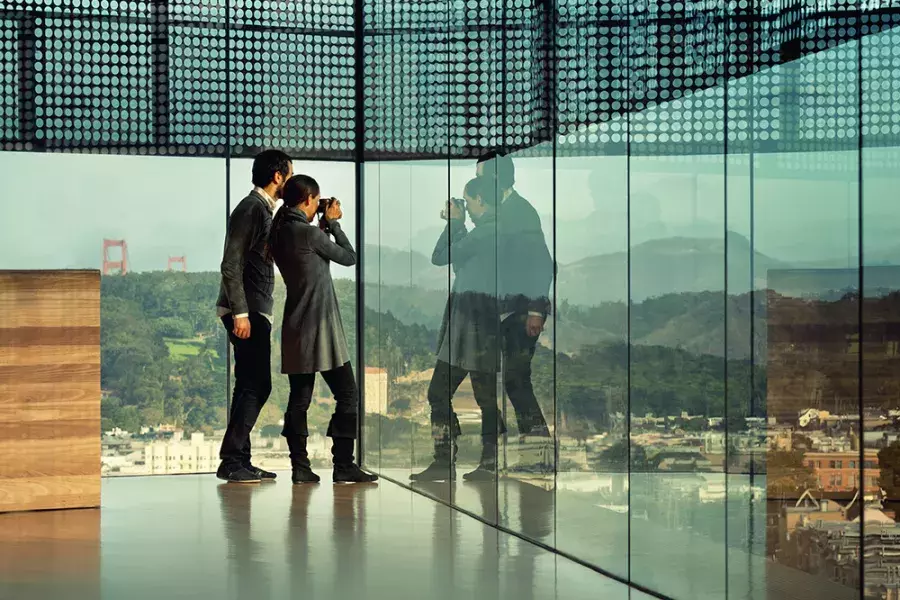 Two people peer through glass walls at the de Young Museum in San Francisco.