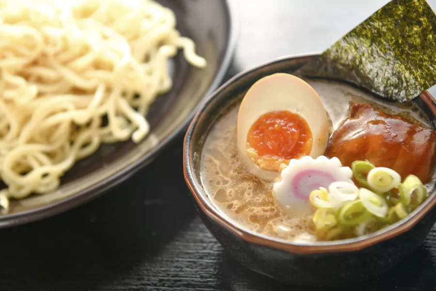 Close-up de uma tigela de macarrão e uma tigela de sopa de ramen com um ovo escalfado, cortado ao meio.