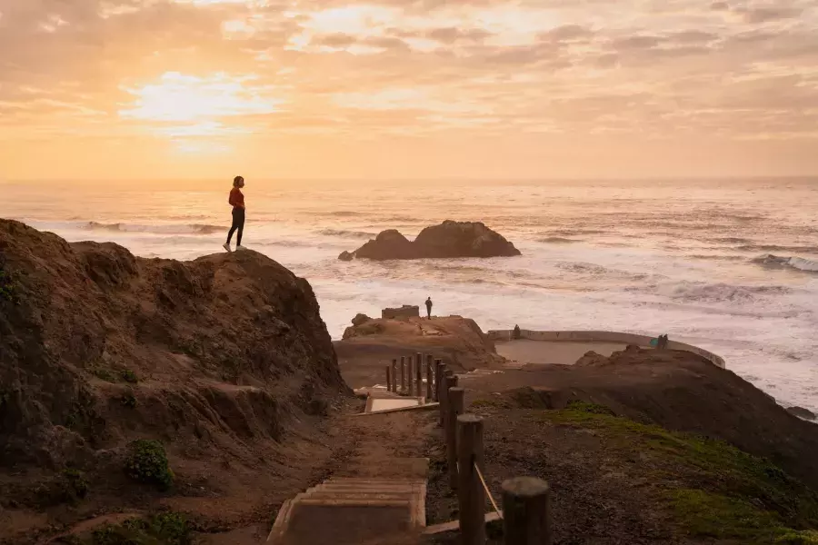 Duas pessoas estão sobre rochas com vista para o oceano em Sutro Baths, em São Francisco.