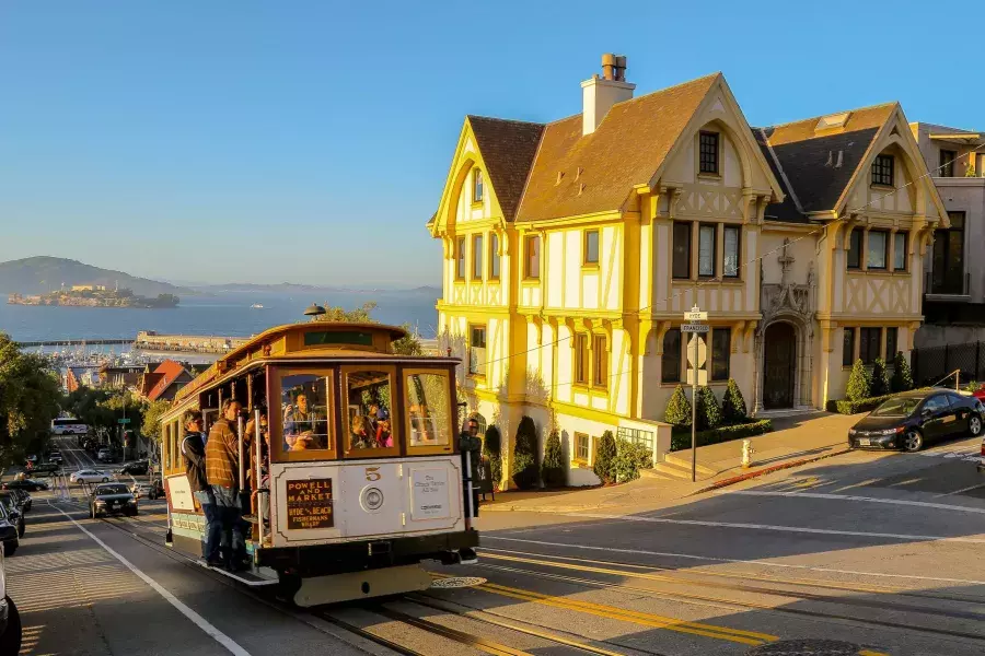 A San Francisco cable car climbs a hill, with Alcatraz visible in the background.