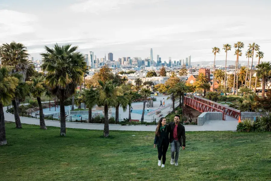 Dolores Parkとサンフランシスコのスカイラインを背に、カップルがカメラに向かって歩いています。