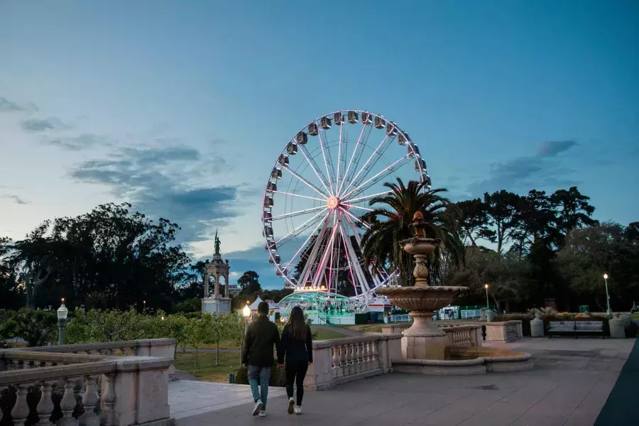 A couple walks toward the SkyStar Ferris Wheel at dusk.