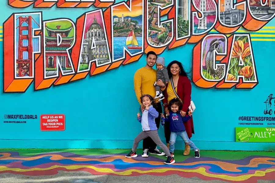 Uma família posando para uma foto em frente a um mural de São Francisco