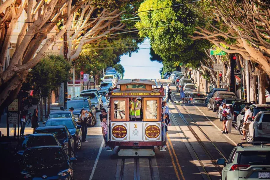 A San Francisco cable car approaches on a tree-lined street.