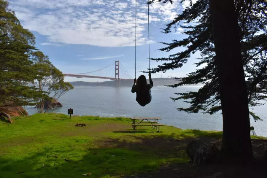 Uma mulher balança em um balanço de árvore com vista para a Ponte Golden Gate. São Francisco, Califórnia.