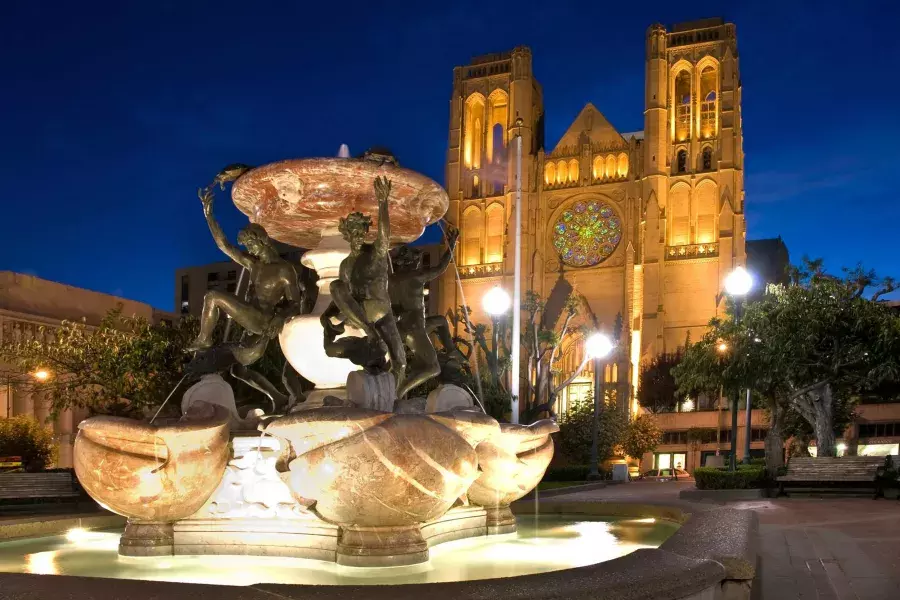 A Grace Cathedral de São Francisco é retratada à noite com uma fonte de água ornamentada em primeiro plano.