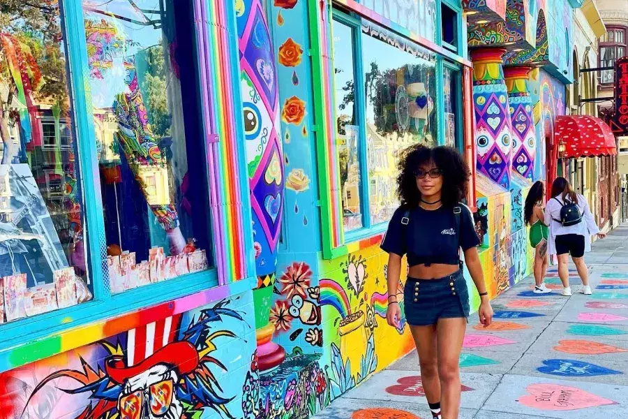 A woman walks down a street with colorful buildings in San Francisco's Haight-Ashbury neighborhood.