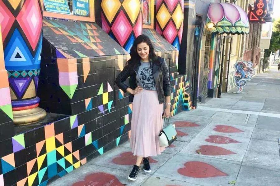 A woman stands on a sidewalk painted with red hearts, in front of a colorful storefront, in San Francisco's Haight-Ashbury neighborhood.