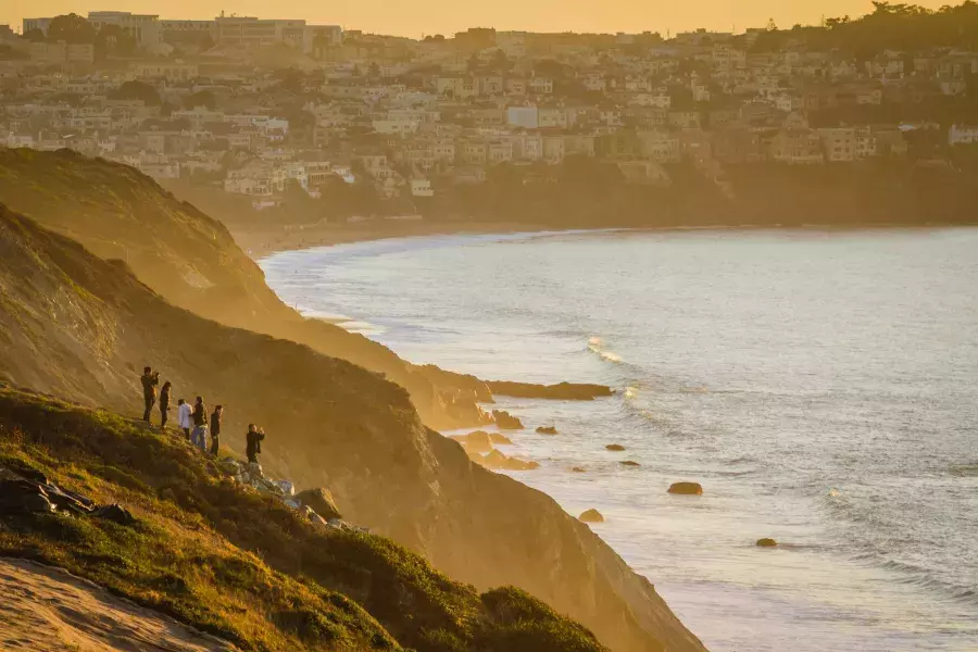 Um grupo de pessoas está à beira de um penhasco à beira-mar observando o pôr do sol no Presidio de São Francisco.