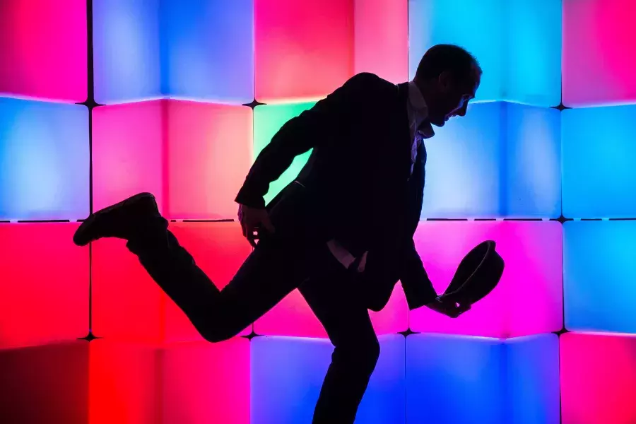 Image of man in front of glowing boxes, posing and lowering hat in a bow position