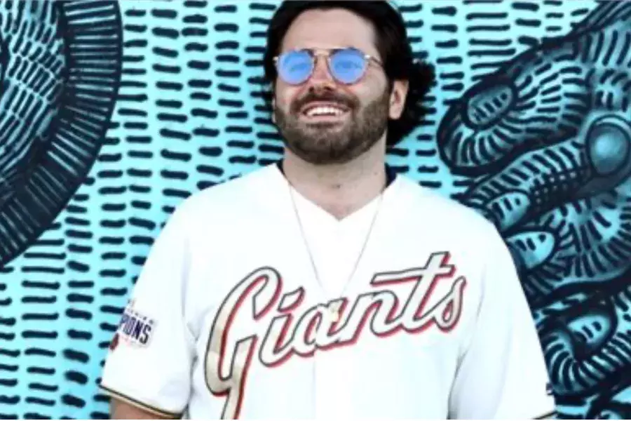 Man in Giants Jersey standing in front of blue mural