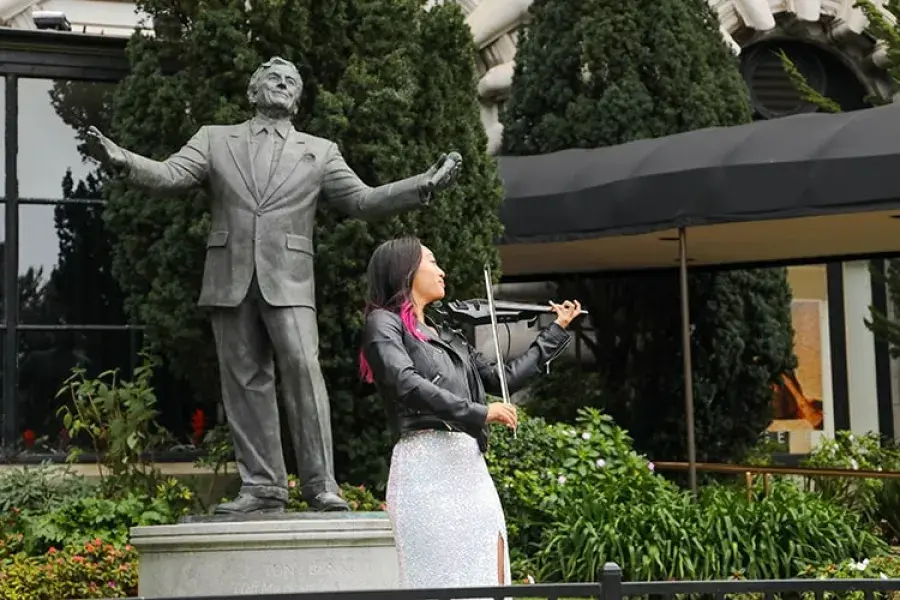 A woman plays the violin in front of the Tony Bennett statue at the Fairmont Hotel.