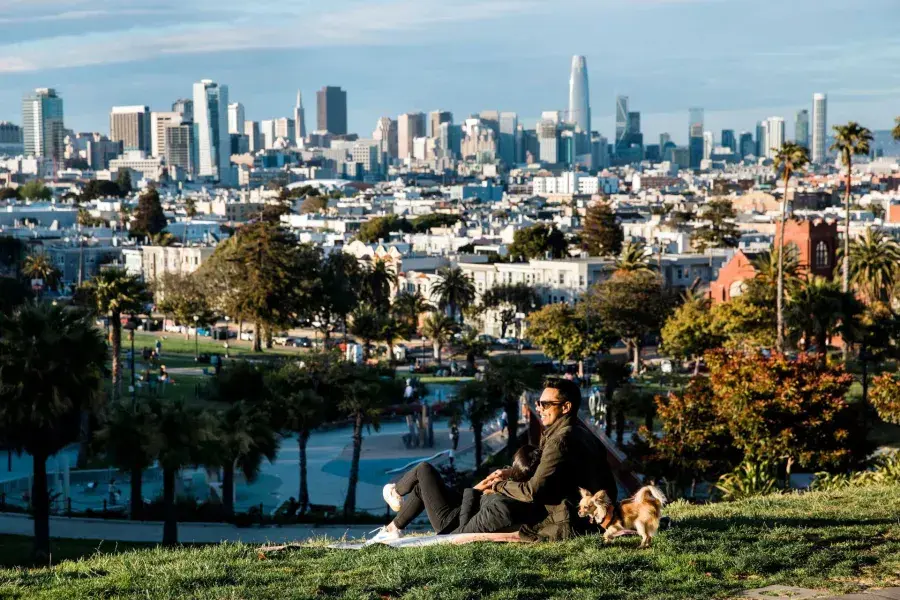 A man and woman sit in an embrace at Dolores Park while gazing at the San Francisco skyline. 