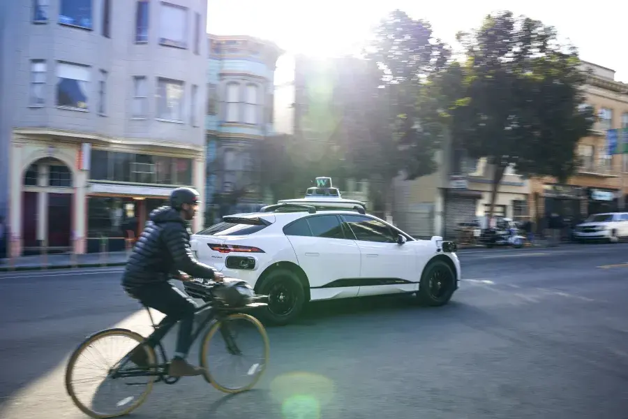 Person riding a bicycle behind a Waymo car