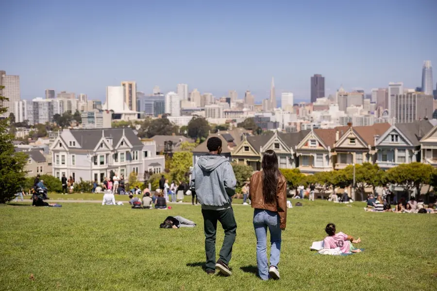 Two people walking in front of the painted ladies in Alamo Square Park